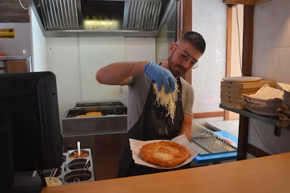 Un bucătar aranjează pe aluat brânză rasă abundentă dintr-un lángos tradițional.